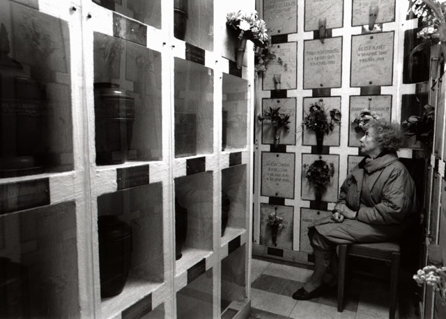 Woman sits in columbarium next to niches with transparent doors