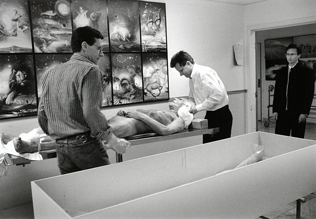 Two sons lifting their dead father to the coffin to be shrouded, signs of the zodiac in the background