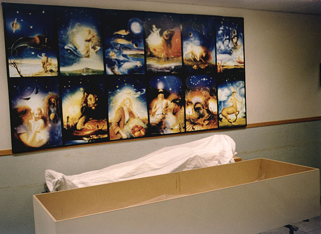Personalen på bårhuset har hängt upp en stor affisch med horoskoptecknien, den toma kistan och ded döda kroppen är framför affischen