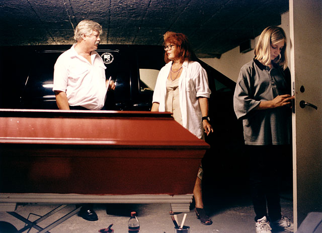 Self painted red coffin, daughter, granddaughter and an undertaker standing next to the coffin