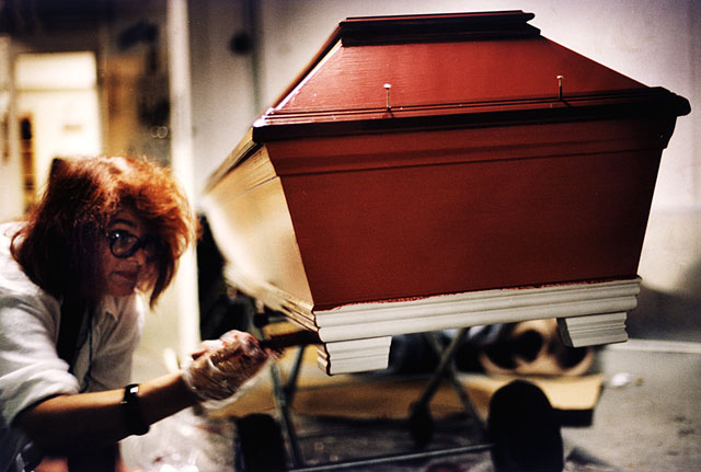Woman with red hair painting her mother´s coffin red