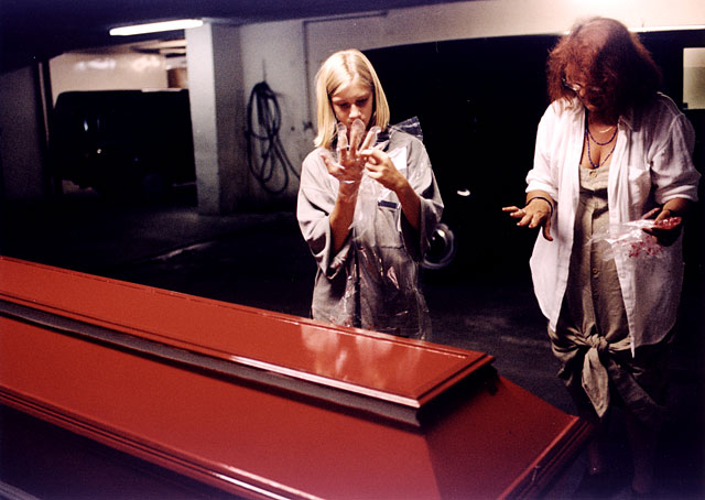 Daughter and granddaughter standing next to the red painted coffin, cleaning their hands