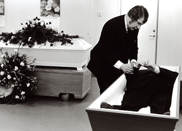 An undertaker shrouding a dead man in a suit