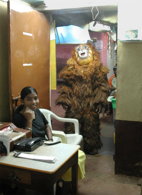 man dressed to a bear, mask and hairy whole body dress standing in the doorway to a phone booth during a festival