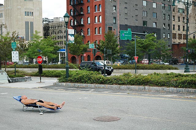 Man sunbathing alone on an empty parking lot with child riding a bike around Chelsie
