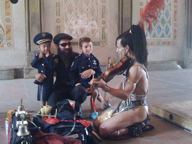 Thoth talking to a man with long beard and sun glasses, holding two young boys in his arms. Boys having police uniforms. Thoth is an extra ordinary very special and multi talented musician and artist