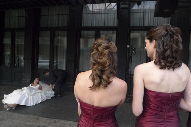 bride laying on the sidewalk, two women watching, wedding naked backs