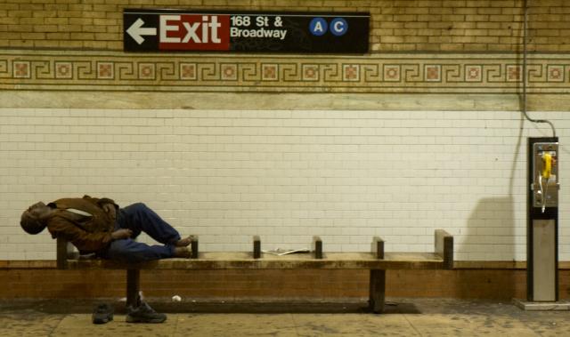Man sleeping on a wooden very uncomfotable bench on the 168th Street subway stop